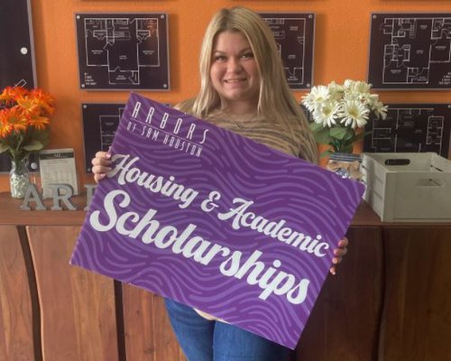 Leasing Specialist holding a sign that reads "Housing & Academic Scholarships"